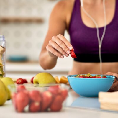 Close-up of female athlete making fruit salad in the kitchen. Close-up of athletic woman adding strawberries while making fruit salad in the kitchen.